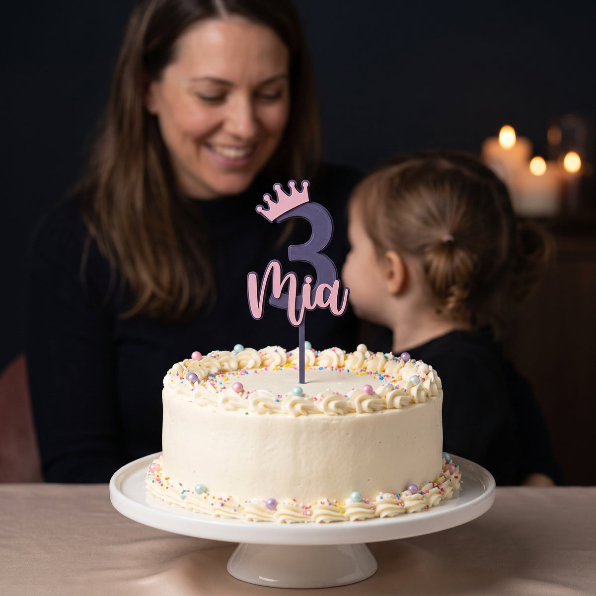 Cake Topper Zahl mit Krone und Name in Indigo und Rosa auf einer Geburtstagstorte, Mutter und Kind im Hintergrund