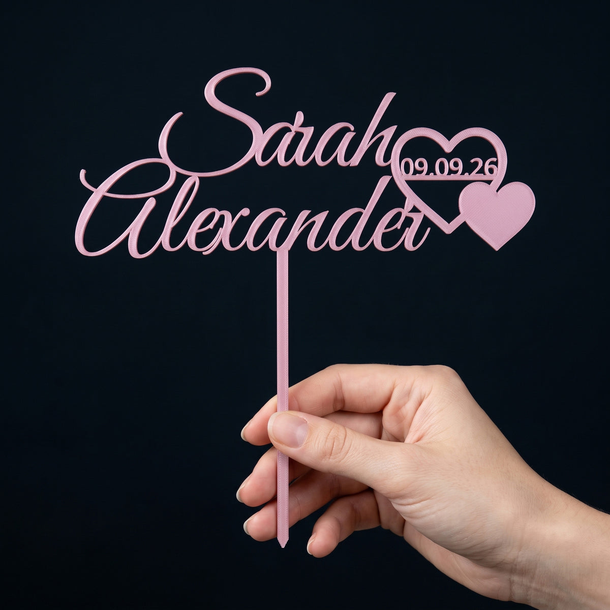 Cake Topper Hochzeit Namen mit Herzpaar in Rosa in der Hand